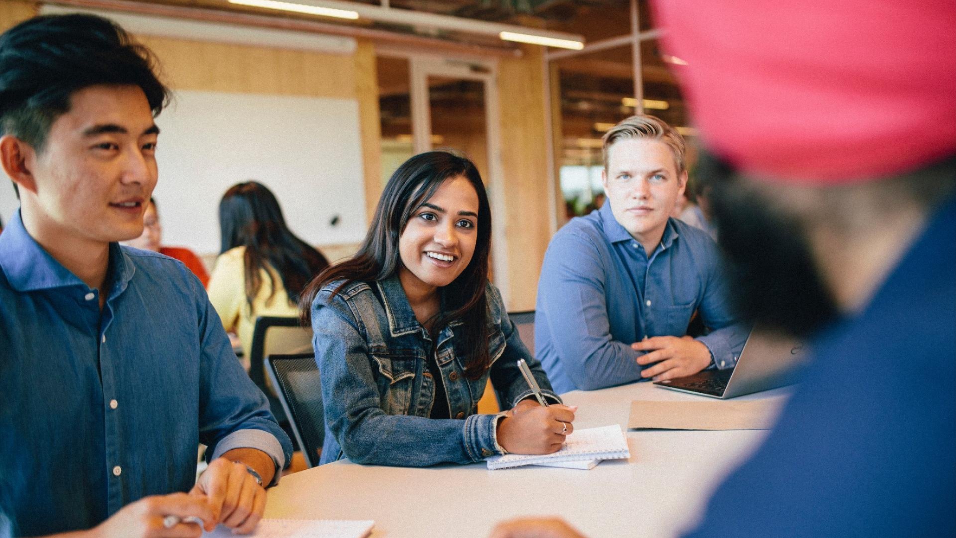 Adults seated in a at a desk during a workshop, smiling and taking notes during a professional development session.