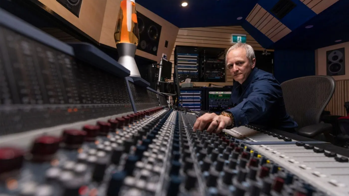 Professor Kenneth Lampl adjusting controls on a large audio mixing desk in a recording studio with speakers and equipment in the background.