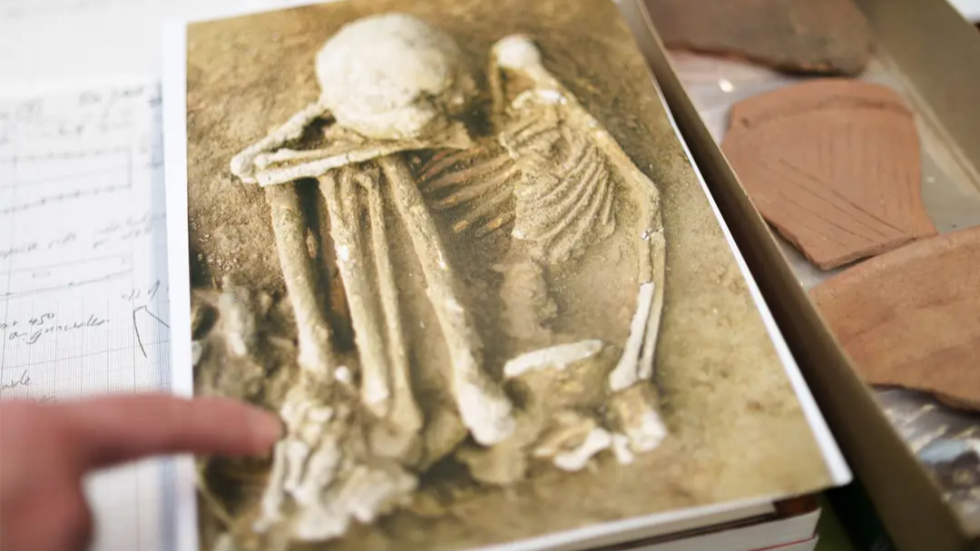 A photograph of an ancient human skeleton displayed on a page, with pottery fragments and archaeological notes around it.
