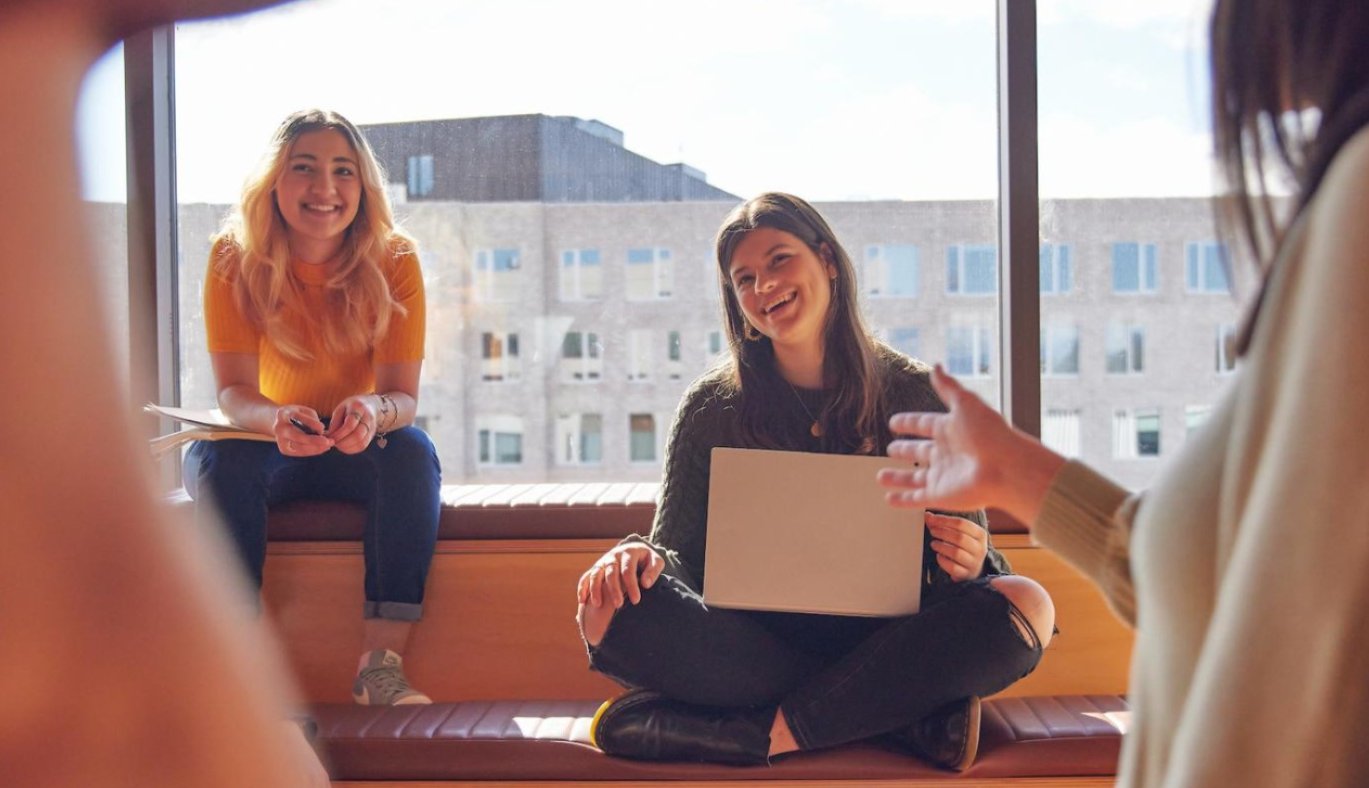 ANU students gather in a sunlit campus space, smiling and chatting as they share ideas.