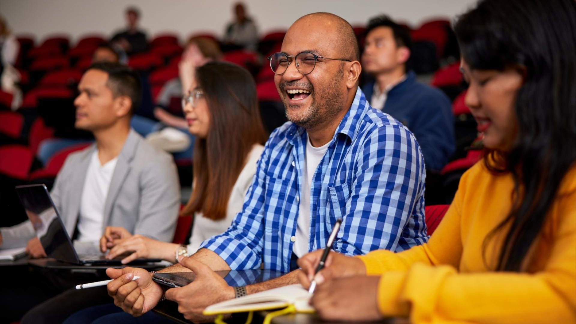 Staff seated in a lecture theatre, smiling and taking notes during a professional development session.