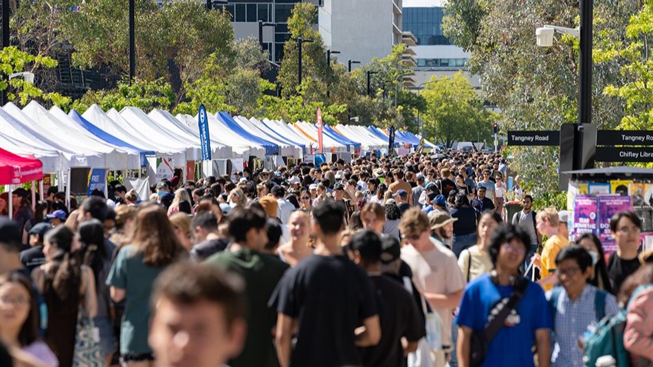 Crowds of students walking past blue market stalls at a busy campus event.