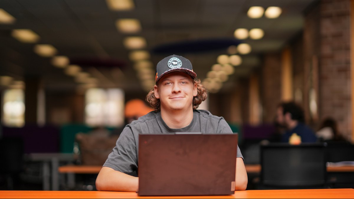 A student studying on a laptop in a campus study space.