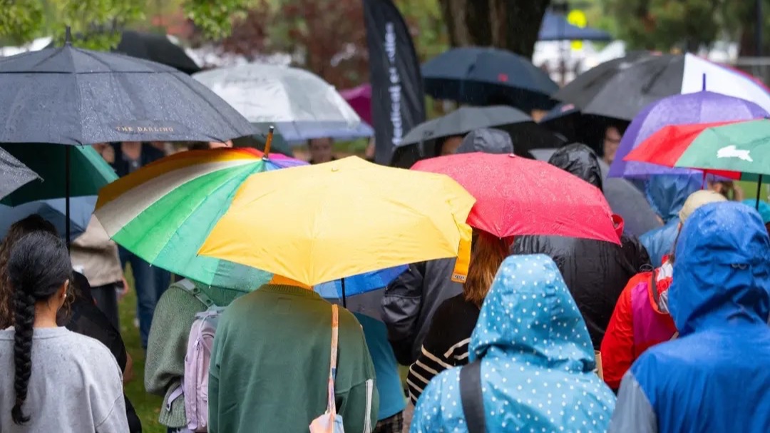 A crowd huddles under colourful umbrellas in the rain. 