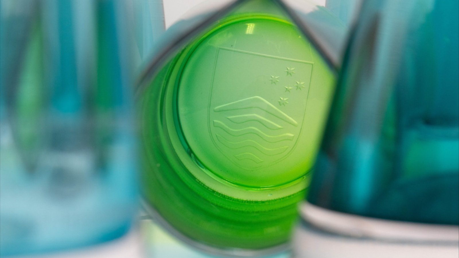 Green ANU shield logo seen through overlapping blue and green translucent award shapes.