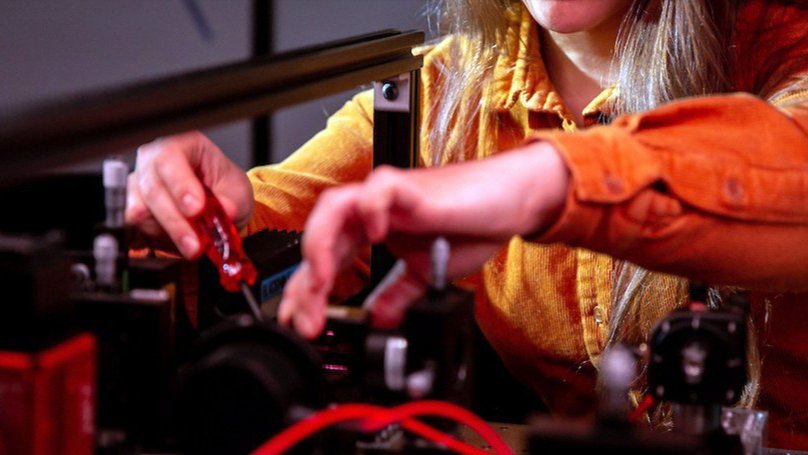 Person adjusting optical equipment with red light in a laboratory.