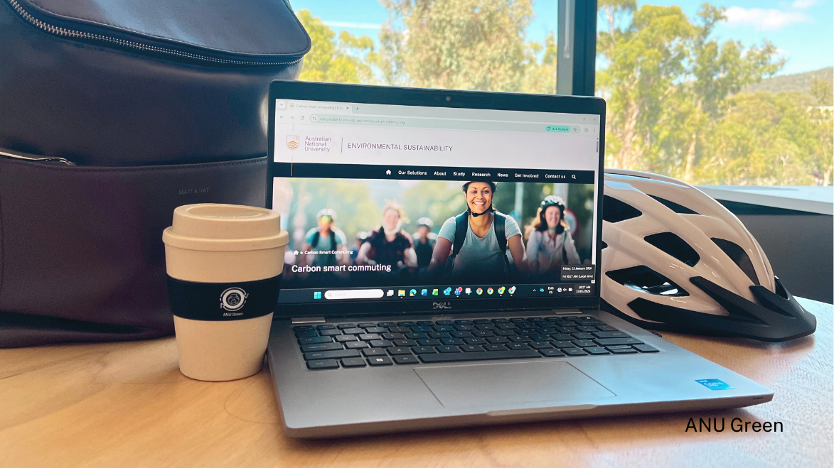Laptop displaying an ��������sustainability webpage on a desk beside a reusable coffee cup, bag and bicycle helmet.