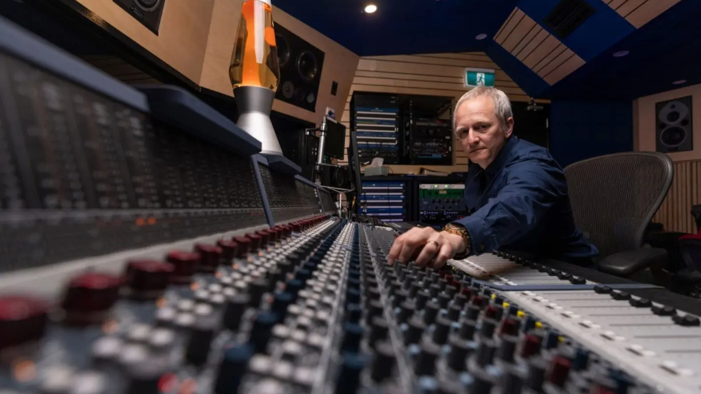 Professor Kenneth Lampl adjusting controls on a large audio mixing desk in a recording studio with speakers and equipment in the background.