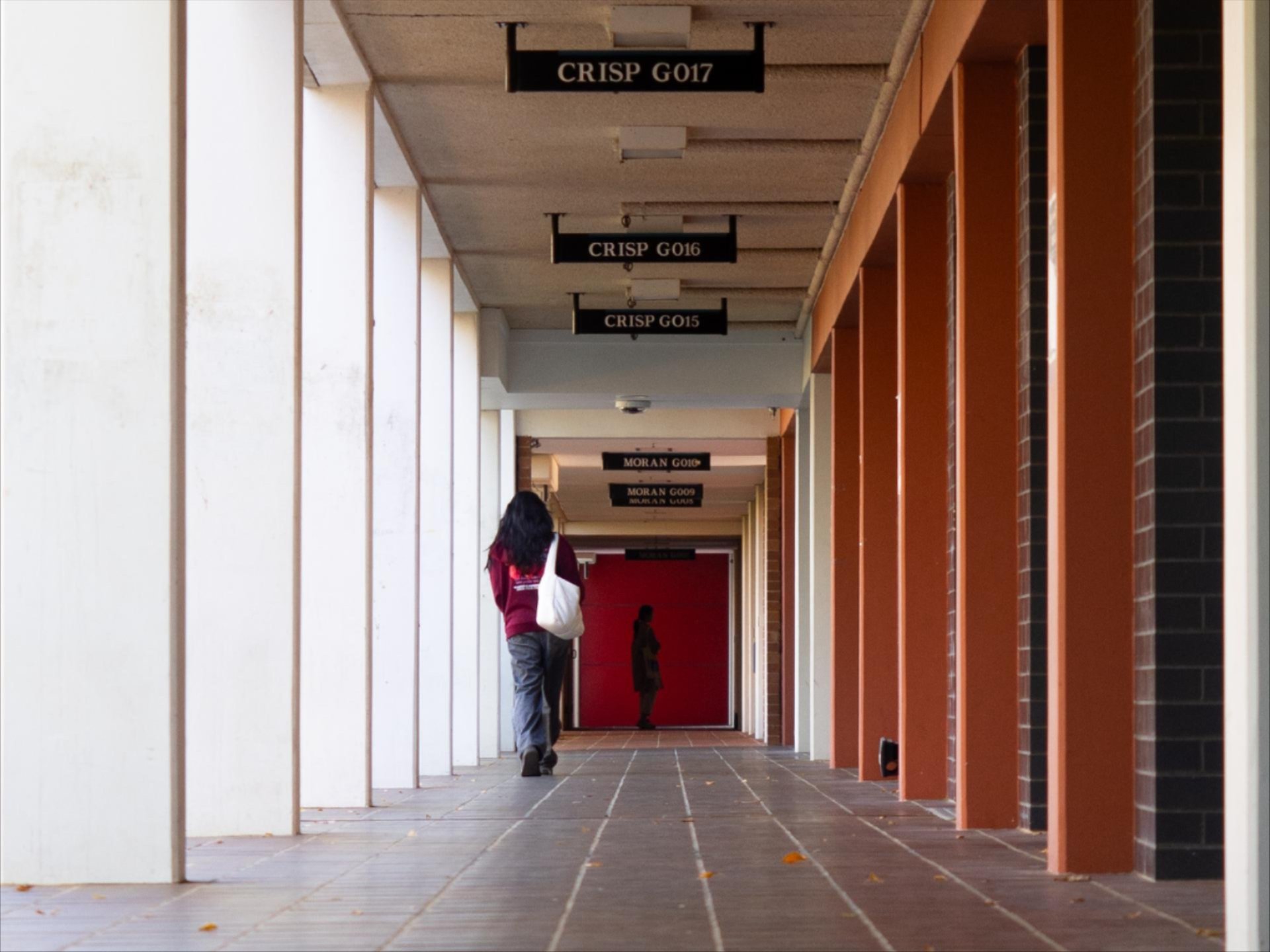 A long, covered campus corridor with repeating concrete columns and windows, receding into the distance and creating a strong sense of perspective.