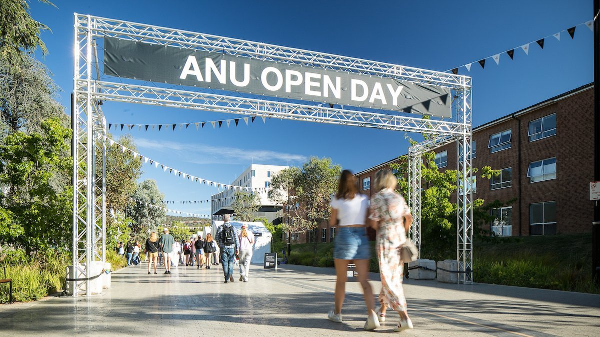 ANU Open Day banner over campus walkway with students walking beneath it on a sunny day.