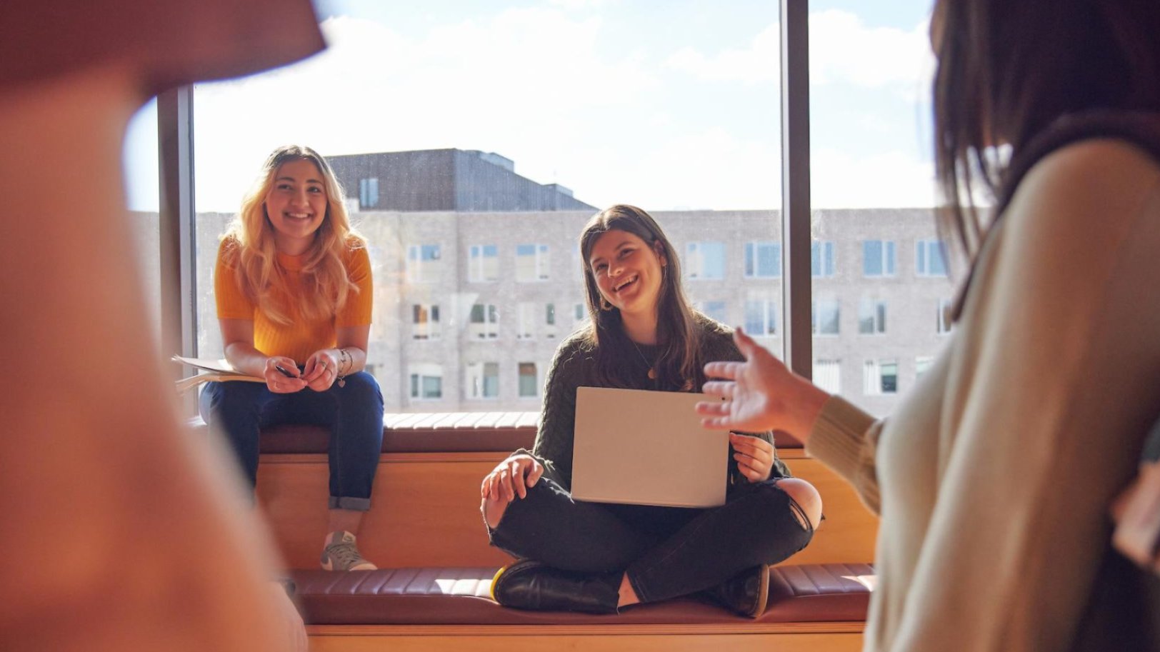 ANU students gather in a sunlit campus space, smiling and chatting as they share ideas, reflecting the supportive and connected community at the heart of life at ANU.