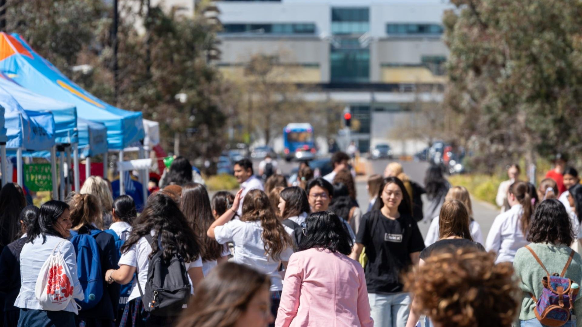Crowds of students walking past O-Week stalls and tents along a busy campus pathway.