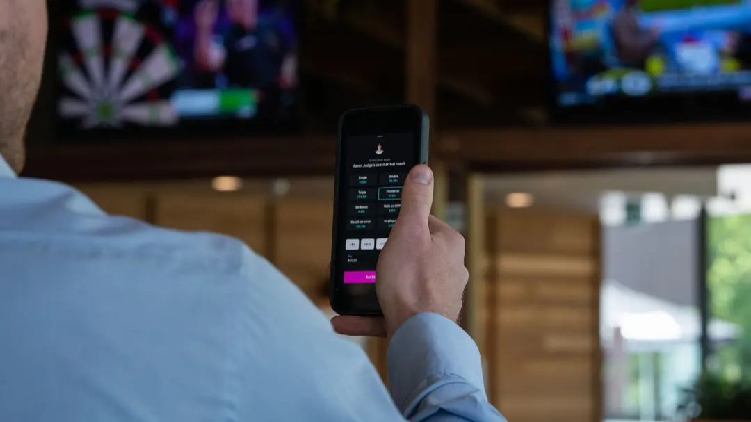 Image of man using phone with gambling app on screen.