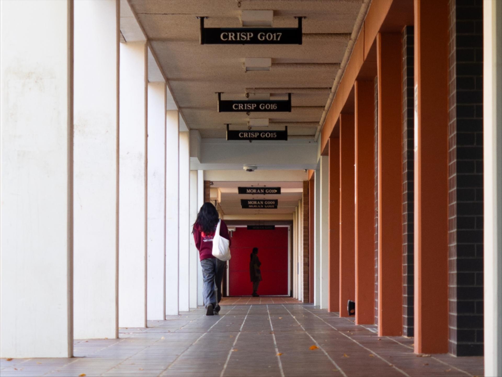 A long, covered campus corridor with repeating concrete columns and windows, receding into the distance and creating a strong sense of perspective.