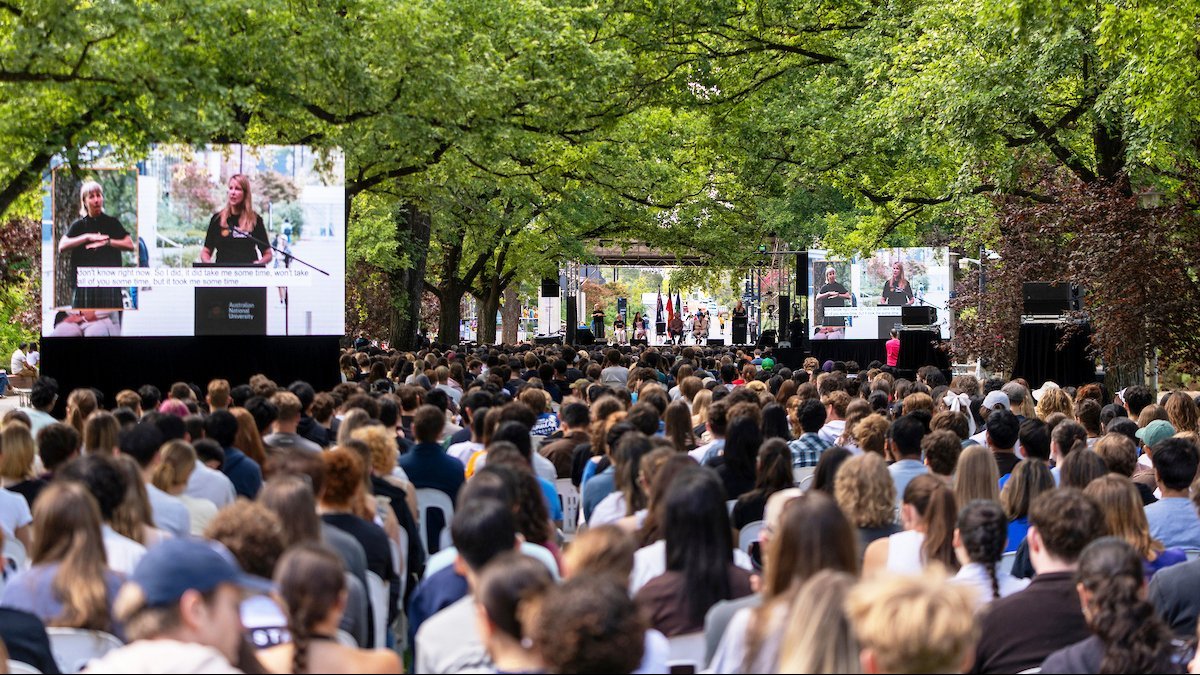 Audience gathered on University Lawn as a speaker delivers the ��������Commencement Address from an outdoor stage.