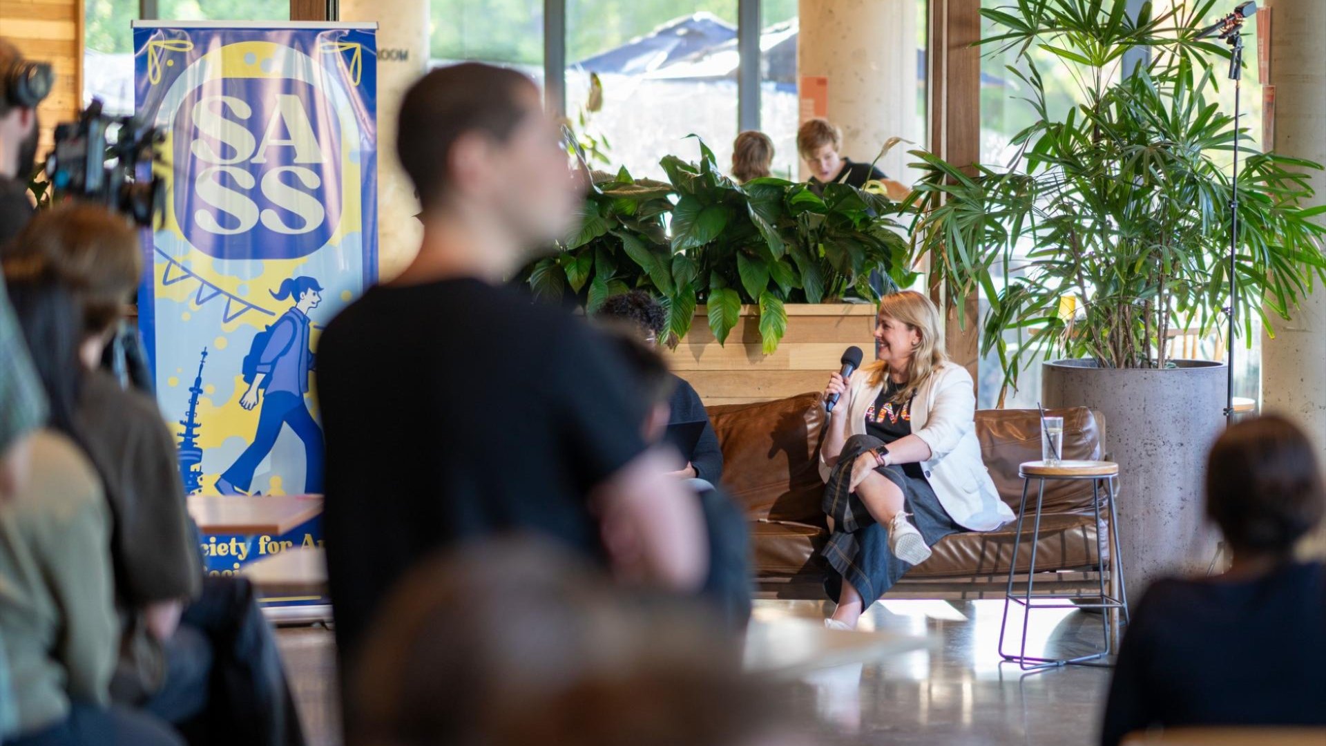 Interim Vice-Chancellor, Professor Rebekah Brown smiles as she discusses the future of ANU at Badger & Co, sitting on a leather couch with a microphone in hand.