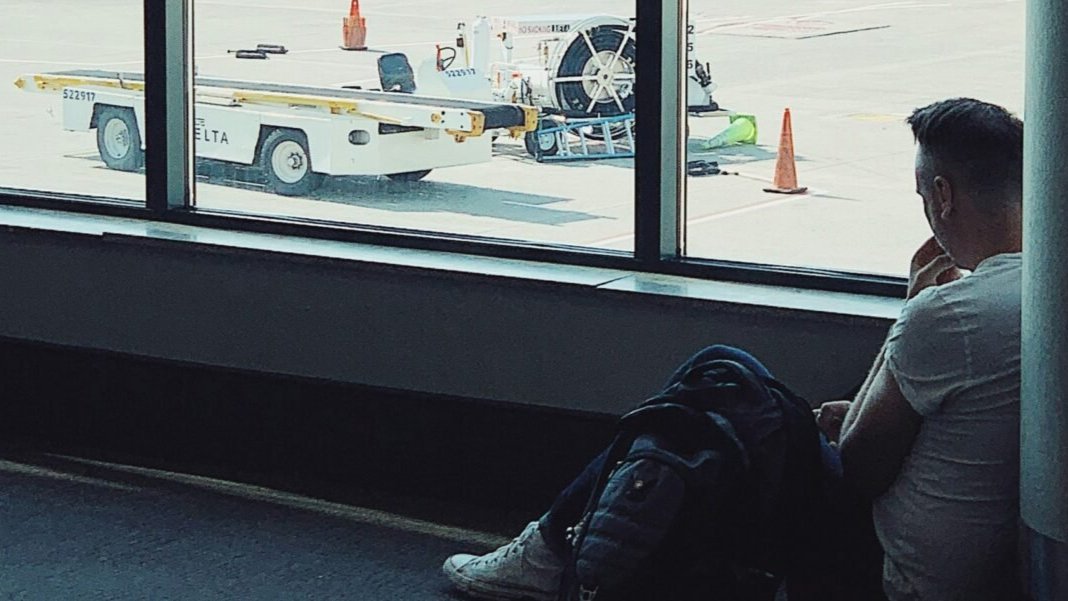 A man sitting on thr ground, waiting in an airport.