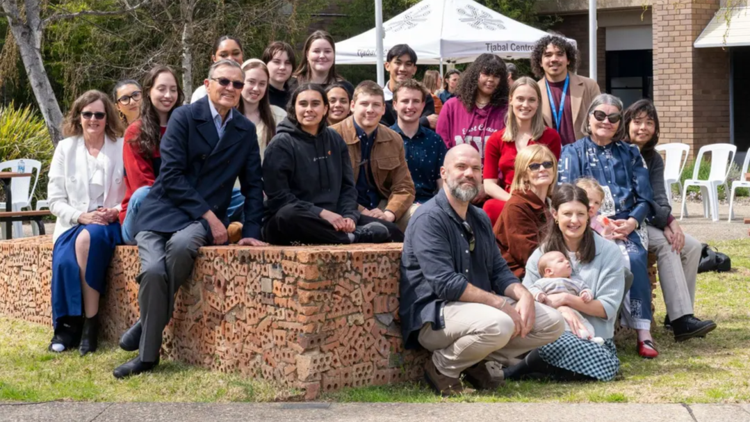Group of Kambri Scholars sitting and standing outdoors on campus, smiling together for a group photo.