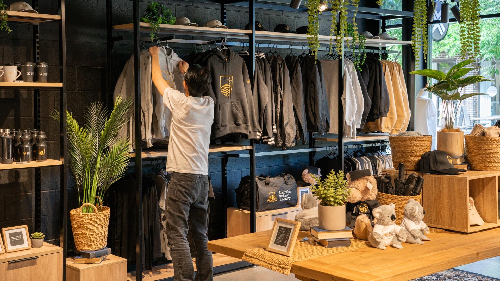 Person arranging clothing on a retail display wall with shelves of clothing and merchandise.