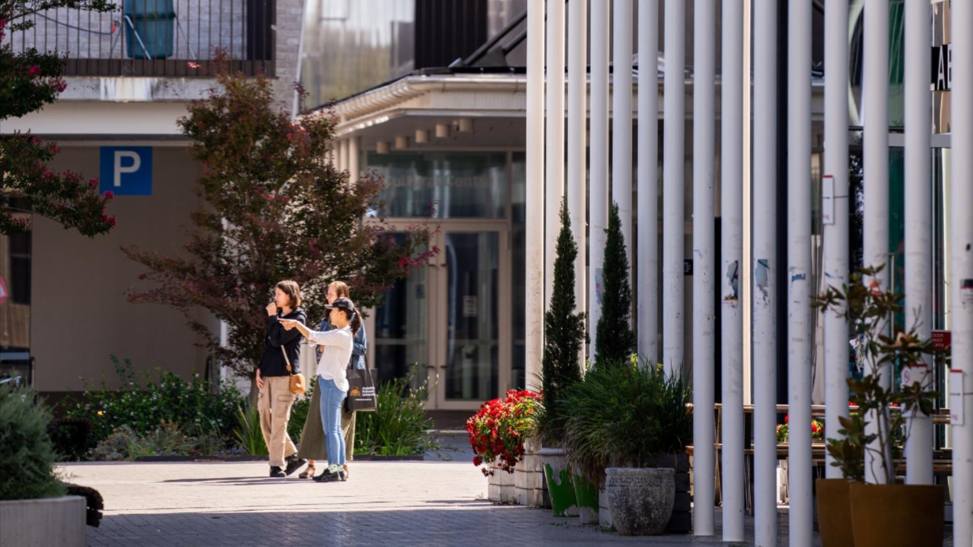 Three people walking outdoors on a sunny day near modern buildings and greenery.