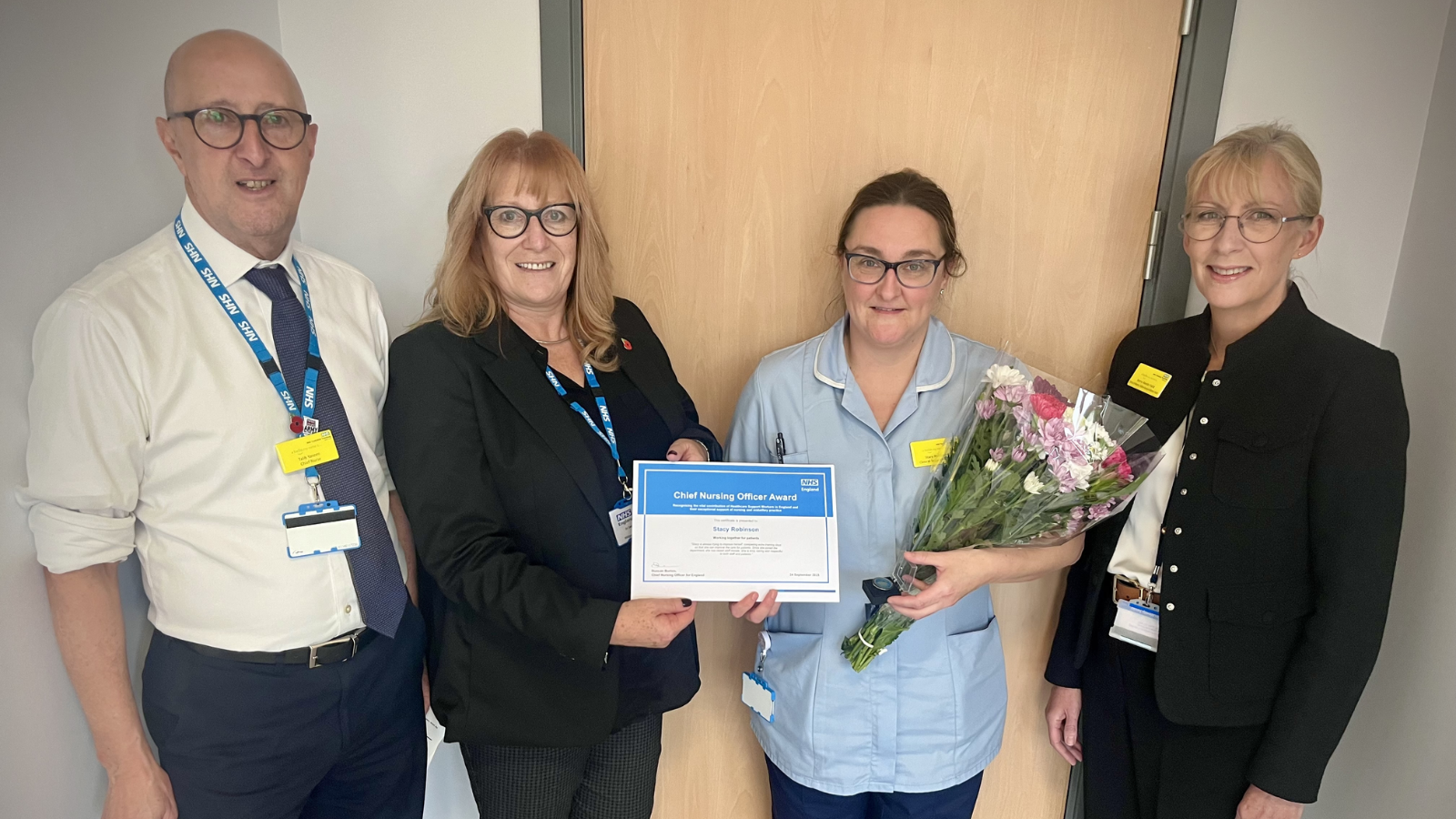 Image of four people, with nurse holding flowers and certificate Image of four people, with nurse holding flowers and certificate