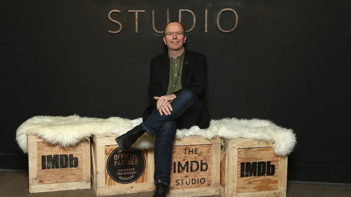 Col Needham sitting on wood boxes that have IMDb logo