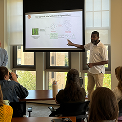 Classroom lecture with speaker gesturing toward presentation screen