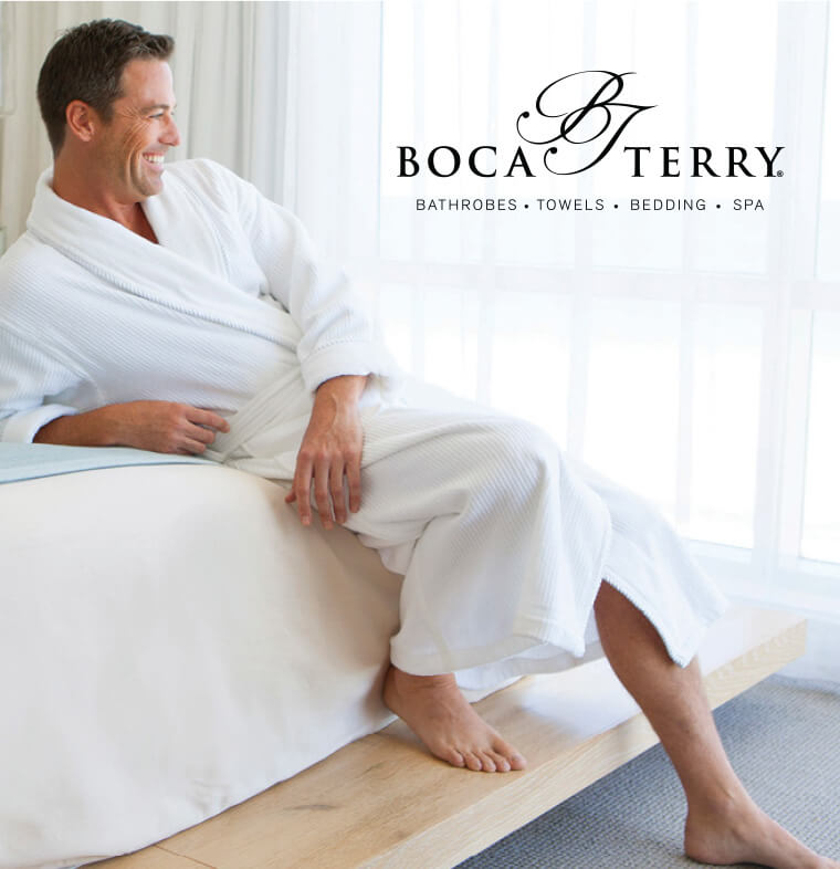 Man relaxing with a smile on bed wearing a white bathrobe.