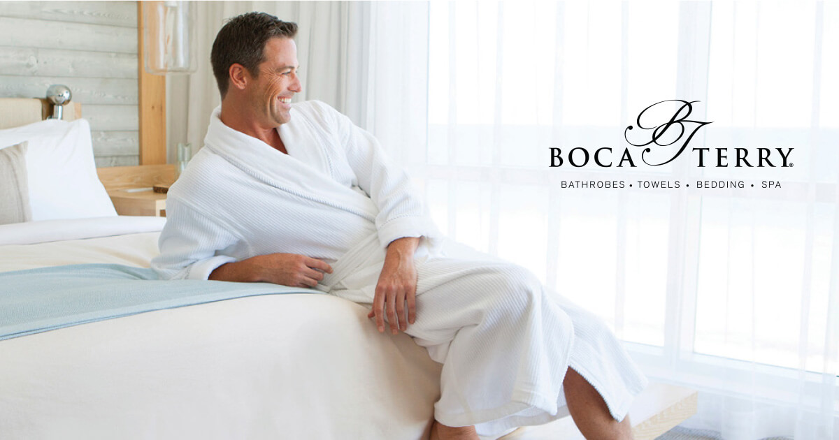 Man relaxing with a smile on bed wearing a white bathrobe.