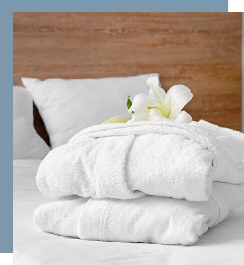 Two white robes folded with an orchid on top laying on top of a bed.