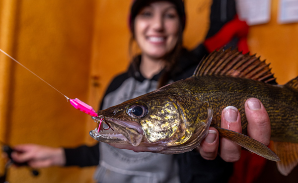 Fisher Jen Pudenz holding walleye inside a fish house