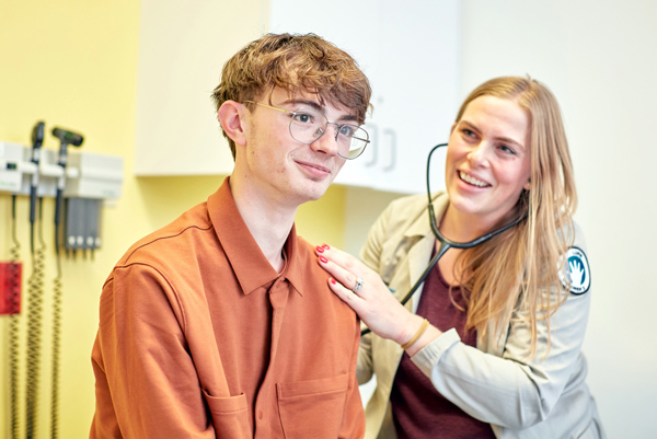 A healthcare professional uses a stethoscope to check a patient during a medical exam in a clinic room.