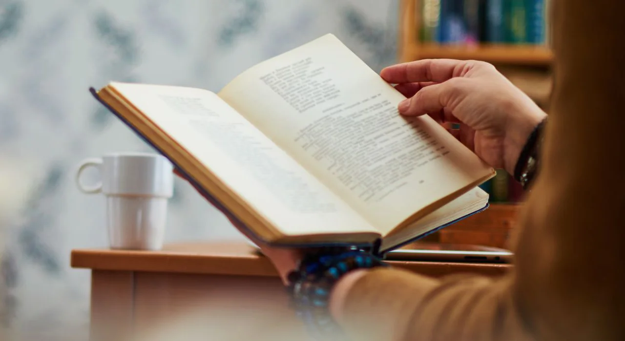 Pessoa lendo um livro, com uma xícara de café à sua frente