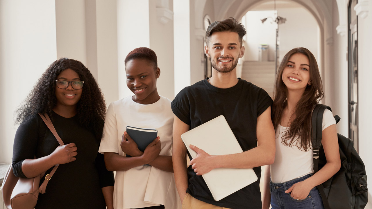 Foto com jovens estudantes, do sexo masculino e feminino, com cadernos e bolsas.