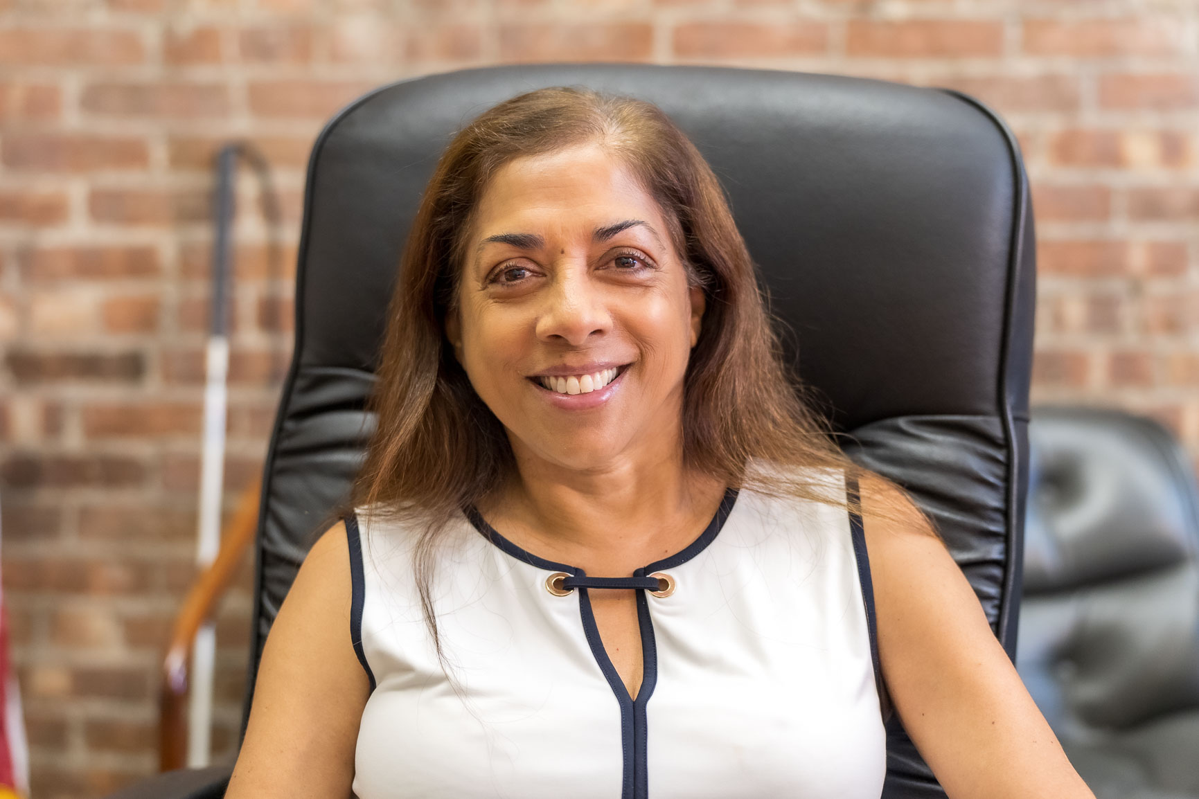 Headshot of Nisha, a woman wearing a white shirt sitting in a black chair smiling to the camera.