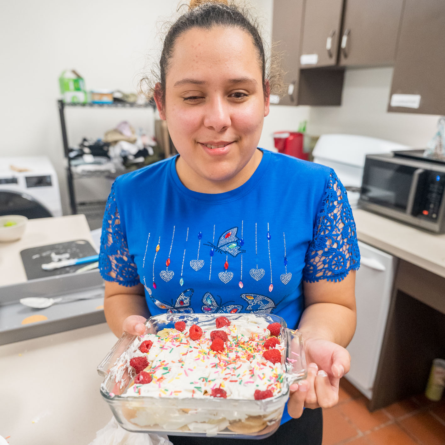 Photo of a young girl smiling to the camera as she holds her hand-made layered cookie dessert topped with Cool Whip, sprinkles, and cherries.