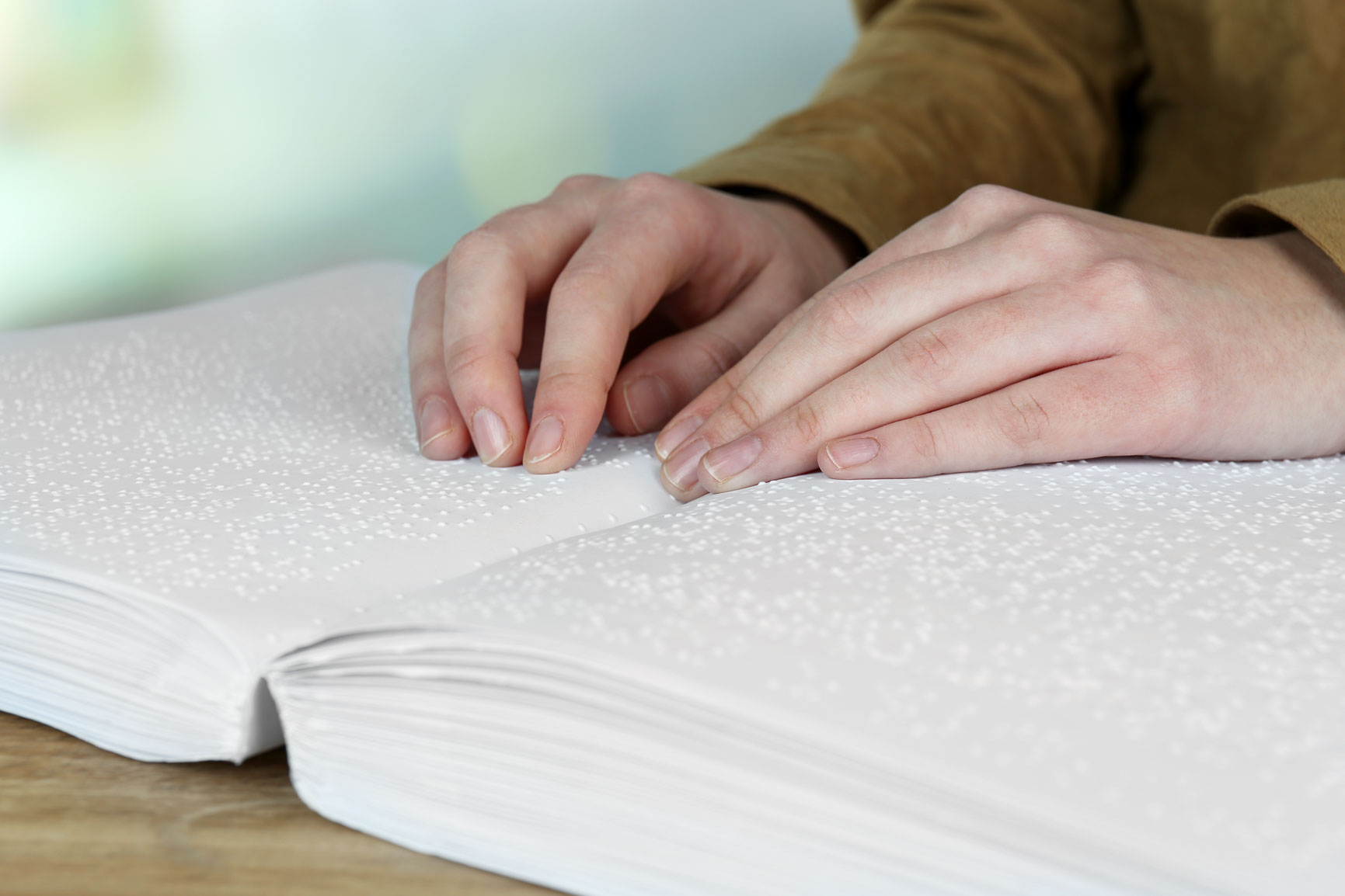 Photo of a woman's hands feeling the Braille characters in a book.