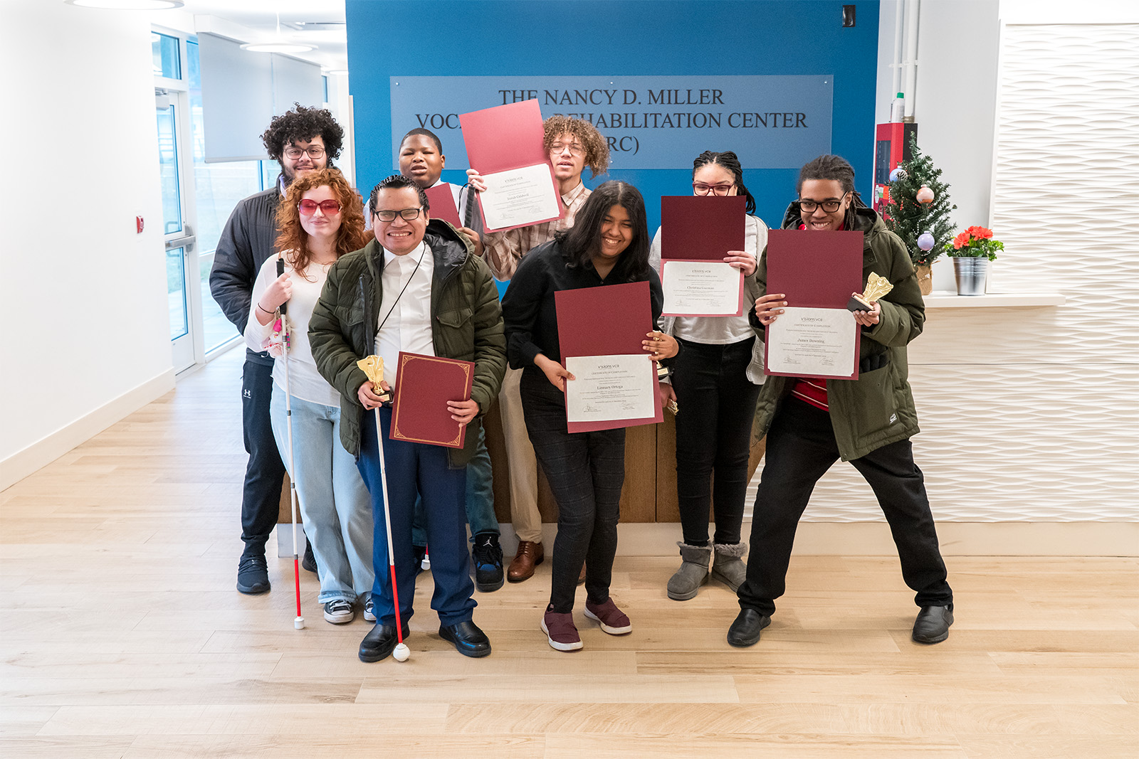 Group photo of young adults standing in the lobby of the VRC, holding their certificates and smiling to the camera.