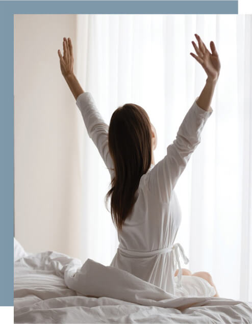 A woman sitting on bed with her arms out stretched.