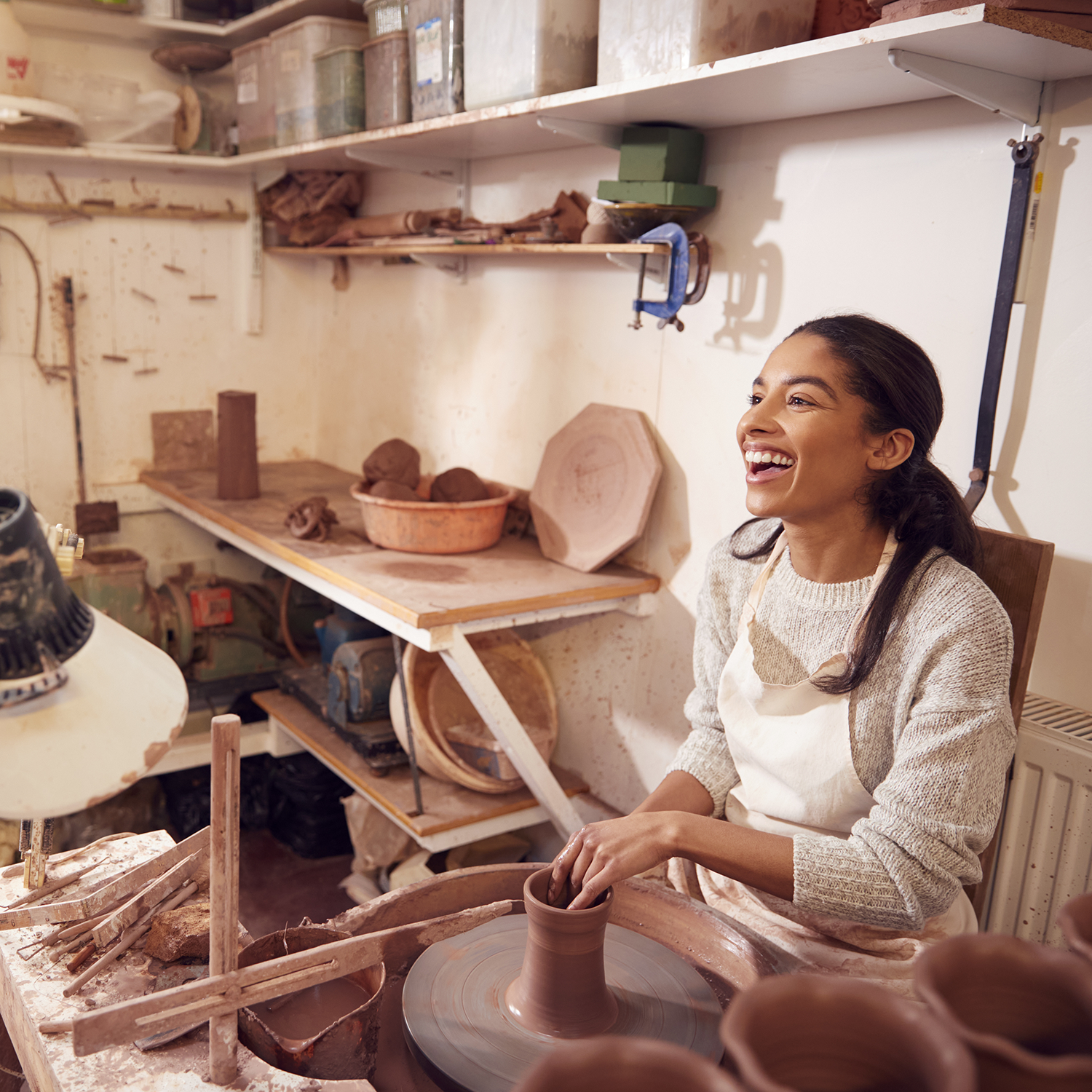 a woman sitting in a workshop at a clay wheel
