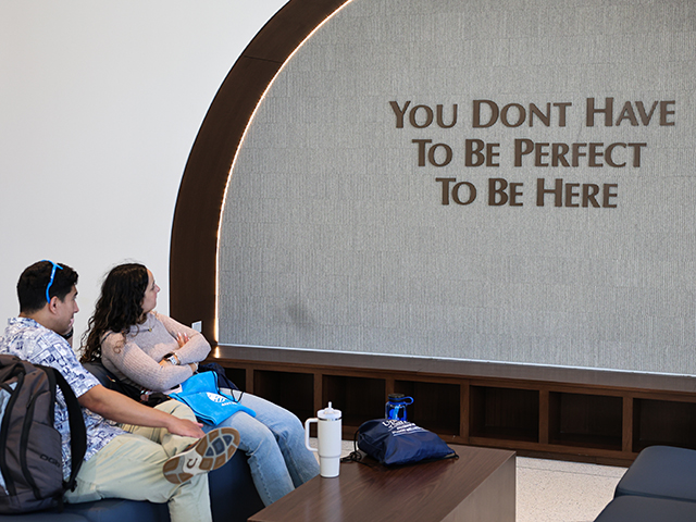 Two students sit and admire a slogan on the wall inside the new Palomar Health Student Wellness Center.