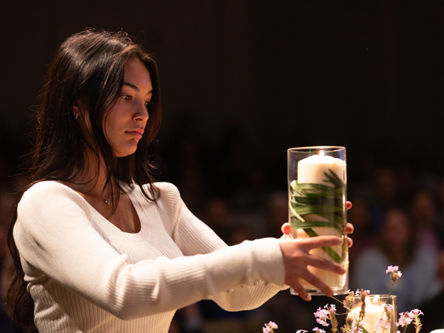 A student places a candle on the alter during All-Faith Service