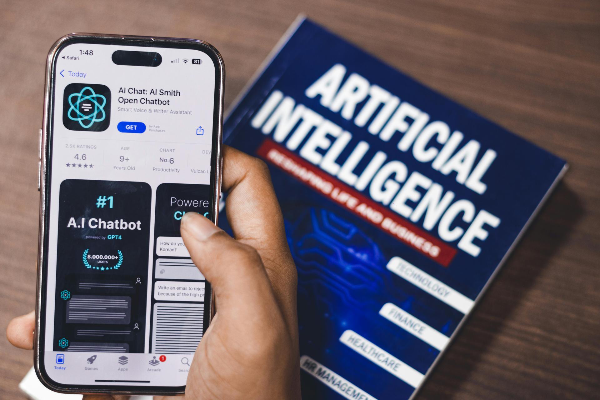 hand holding phone, book that reads 'Artificial Intelligence'