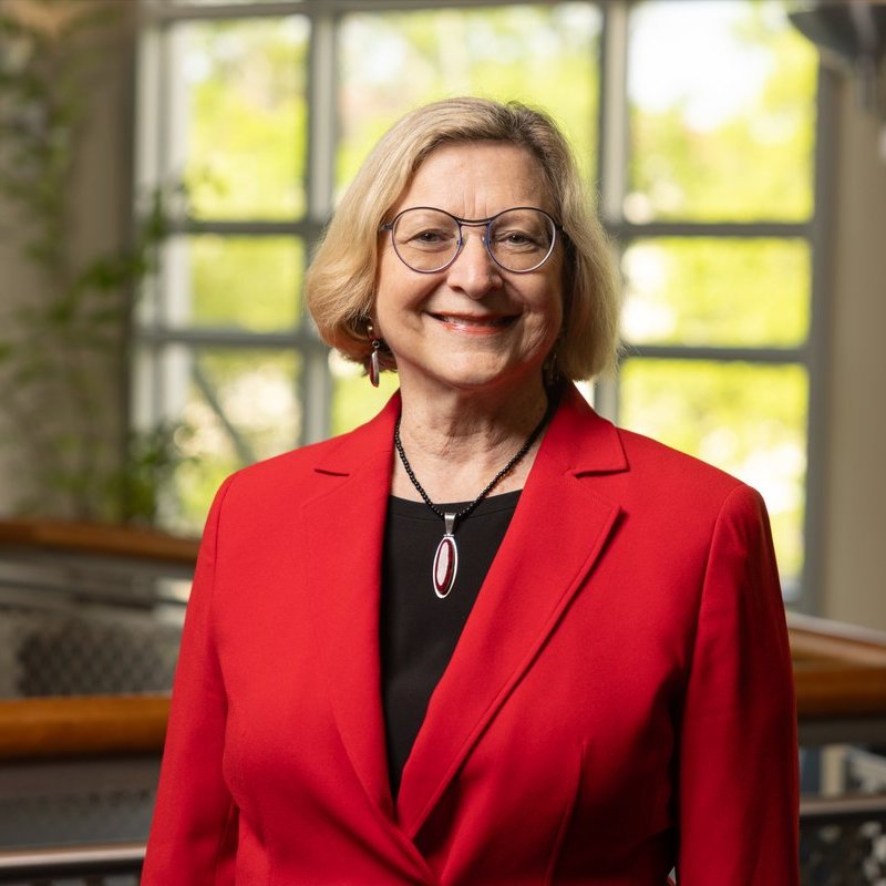 Portrait of Dean Appel standing in front of a window, wearing a read jacket