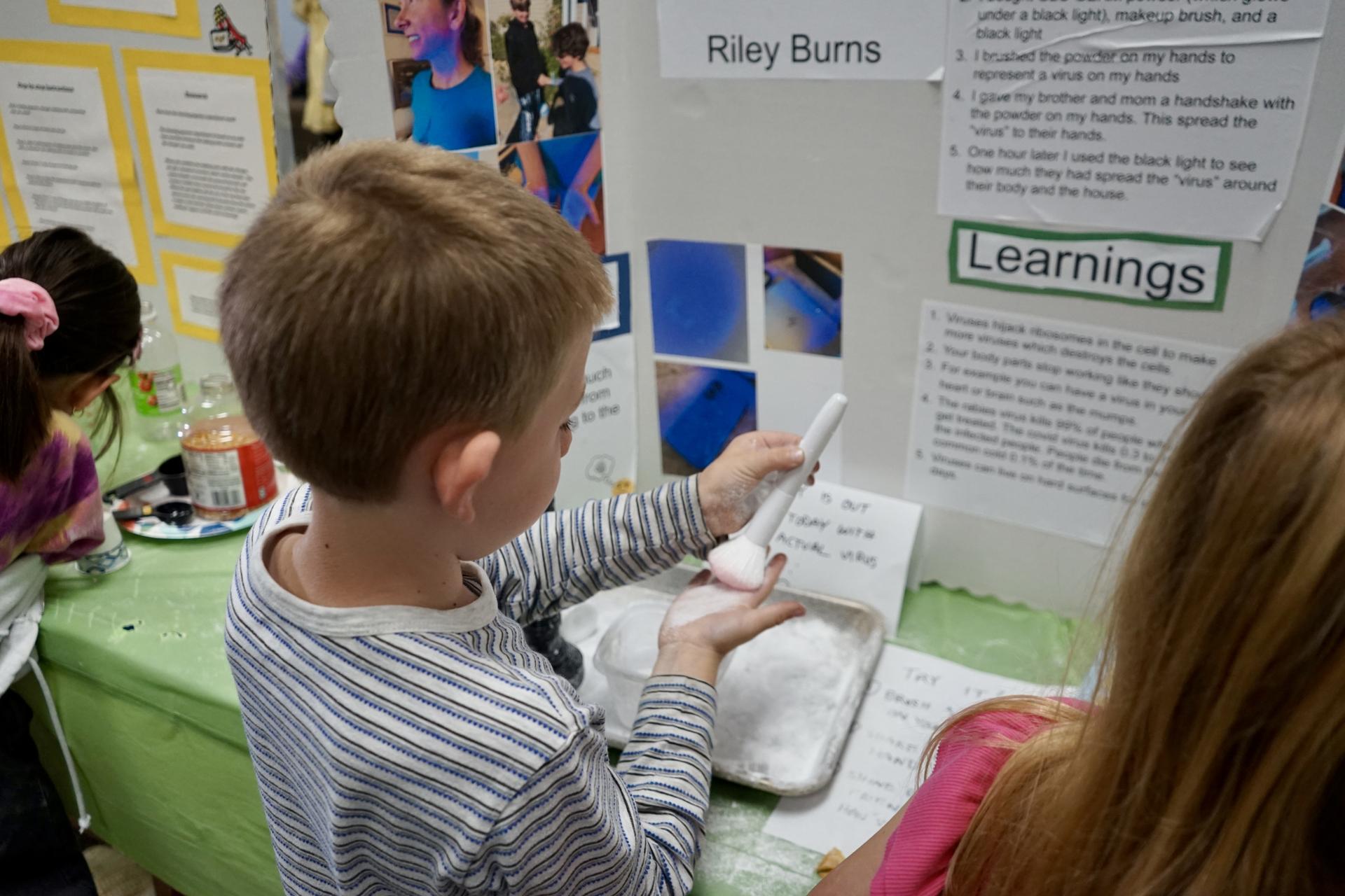 A student is shining a flashlight on their hand as part of an interactive science fair project display.
