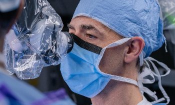 Norberto Andaluz wears a scrub cap and mask while looking through a microscope during surgery