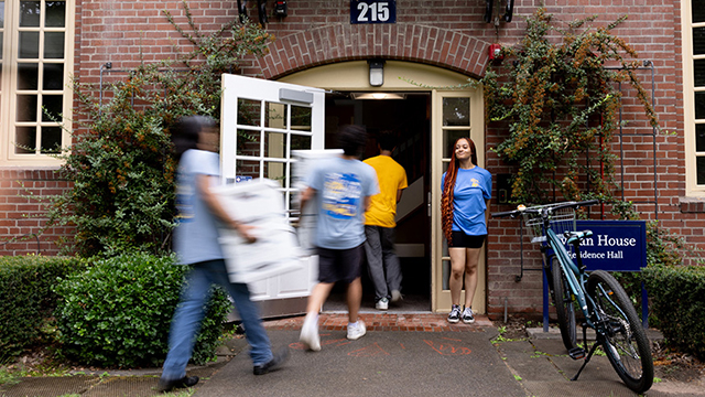 A group of people carry boxes in through the entrance to a residence hall.