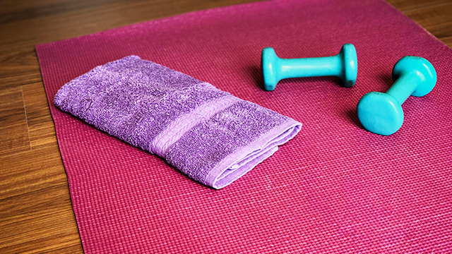 A red exercise mat with a purple towel and two teal dumbbells.