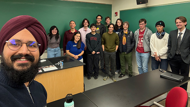 A group of students, staff and faculty take a selfie in a classroom.