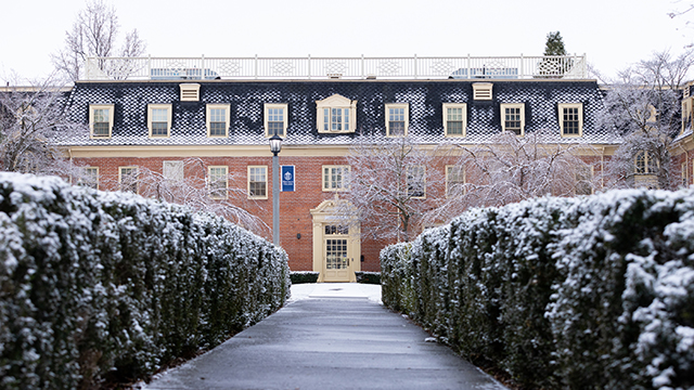 A hedge-lined sidewalk, lightly covered with a thin layer of snow, leads to Prentiss Hall.